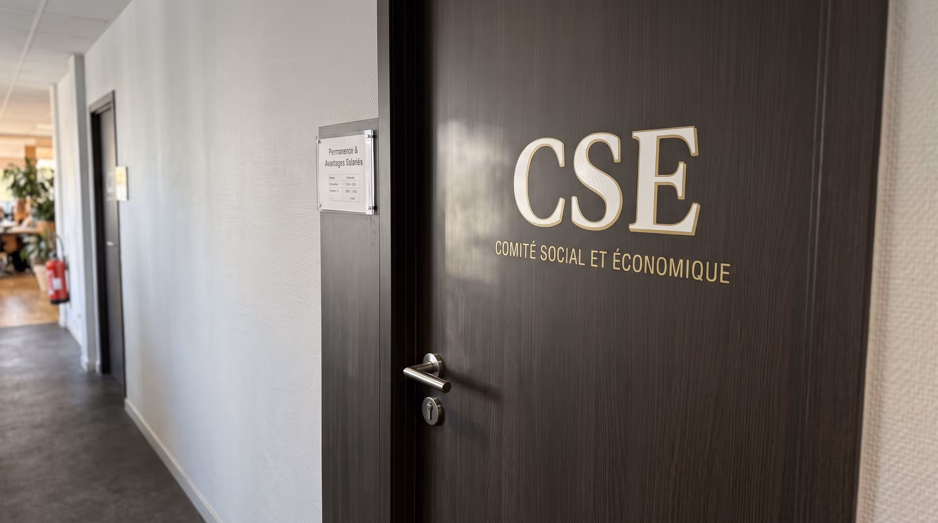 Porte de bureau en bois sombre affichant l'inscription « CSE - Comité Social et Économique » dans un couloir d'entreprise.